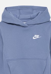 Svijetloplavi Nike hoodie s prednjim džepom, kapuljačom na vezanje i malim bijelim logotipom na gornjem lijevom dijelu prsa. Mekana tekstura.