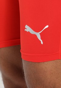 Červené sportovní šortky s těsným střihem. Na spodní straně je velké, reflexní stříbrné logo Puma. Hladká, elastická tkanina.