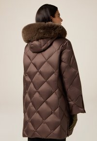 Braune gesteppte Steppjacke mit pelzbesetzter Kapuze. Verfügt über eine lockere Passform, diagonale Steppnähte und seitliche Reißverschlusstaschen. Die Textur wirkt glatt.