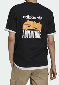 Czarny bawełniany T-shirt z białymi wykończeniami, dużą grafiką gór oraz krętej drogi w kolorze pomarańczowym z napisem "PRZYGODA" w grubym białym tekście.