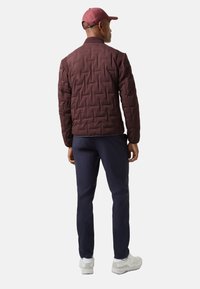 Bordeauxrote gesteppte Jacke mit einer strukturierten Musterung, geripptem Kragen und passender Mütze. Kombiniert mit einer marineblauen Hose und weißen Turnschuhen.