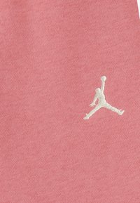 Roza pamučna tkanina sa bijelim izvezenim Jumpman logom, koja prikazuje ikoničnu siluetu branda u dinamičnoj pozi.