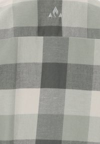 Ternet skjorte med skiftende lysegrønne, mørkegrønne og hvide felter, lavet af et blødt stof med et broderet logo over halsudskæringen.