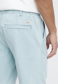 Lys blå bukser i stof med elastisk liv. Har en baklomme med etikett, glat tekstur og rett ben-design.