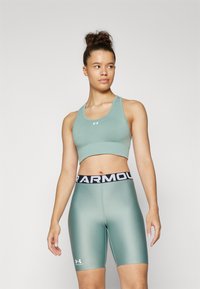 Top cropped atlético verde claro e calções de bicicleta a condizer, com uma faixa na cintura preta com o logótipo "Under Armour" e um tecido liso e elástico.