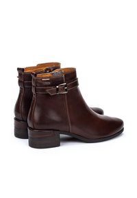 Botas de tobillo de cuero marrón con un acabado suave, tacón bajo y una correa decorativa con hebilla. Forradas con un material de contraste en tono beige.
