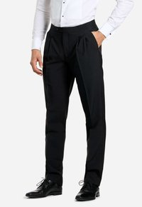 Pantalones formales negros con pliegues, confeccionados en tela suave, con bolsillos laterales y un ajuste entallado. Combinados con una camisa blanca y zapatos negros.