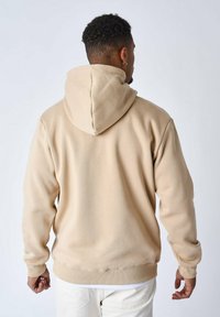 Sudadera con capucha beige de textura suave, con un corte holgado y puños acanalados. Diseño limpio sin patrones visibles ni elementos metálicos.