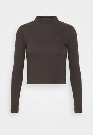 Pruun, pikkade varrukatega, lühendatud turtleneck särk, mis on valmistatud ribakujulisest kangast. Sellel on vasakul rinnal diskreetne logo.