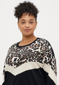 Lepardo raštas sportinė palaidinė su kontrastiniu juodu apačiu ir grietinėlės spalvos zigzaginiu ornamentu. Pagaminta iš minkštos medžiagos, laisvai krentanti.