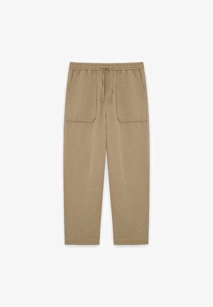 Beige casual broek met elastische tailleband, trekkoord en twee grote voorzakken, plat weergegeven op een witte achtergrond.