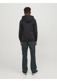 Svart huvtröja med en stor bakficka, i kombination med mörkgröna cargobyxor med sidofickor och vita sömdetaljer.