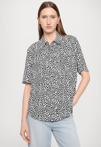 Short-sleeve button-up shirt in black and white with a polka dot pattern, featuring a relaxed fit and two chest pockets.