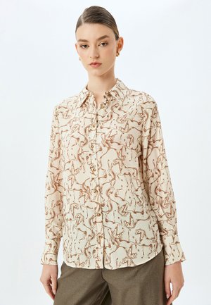 Mønstret bluse i beige med brune hestemotiver, der har knaplukning foran, krave og lange ærmer lavet af letvægtsstof.