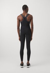 Fekete sportos ujjatlan felső fehér díszítéssel, fekete leggings-szel kombinálva. Testhez simuló fazon, versenyhát kialakítással. Fekete sportcipővel viselve.