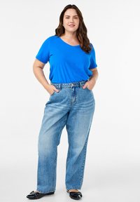 Modrý tričko s V výstřihem v kombinaci s vysokými světle modrými džíny. Džíny mají volný střih a outfit doplňují černé balerínky.