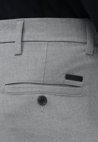 Gros plan sur la poche d’un pantalon gris sur mesure avec un bouton noir et une petite étiquette de marque noire sur le tissu.