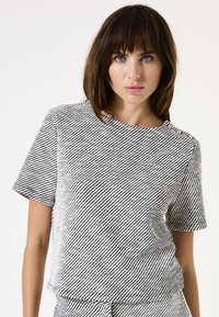 Top de manga corta a rayas en blanco y negro con un corte relajado. Presenta un escote redondo y botones en el hombro. Textura suave.