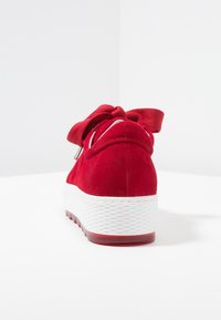 Baskets en daim rouge avec une semelle blanche texturée, dotées d'un nœud en ruban de satin et d'un design arrière arrondi.