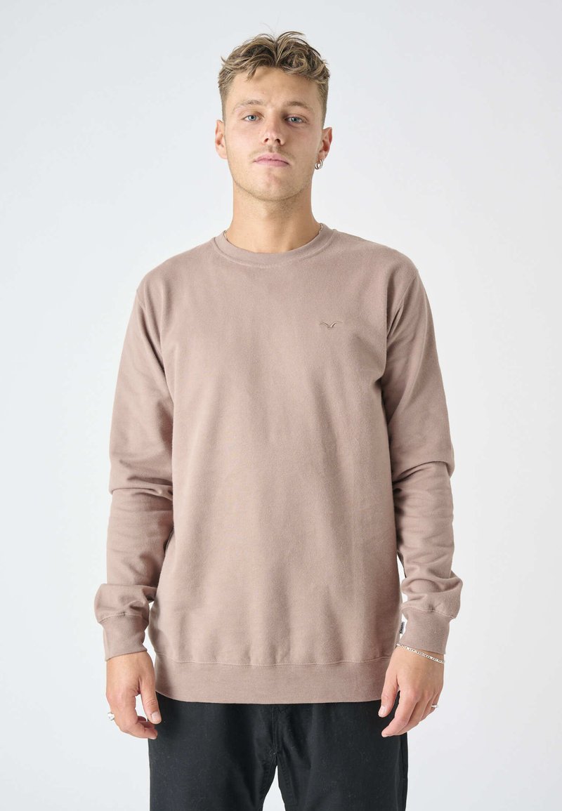 Light brown long-sleeve sweatshirt with crew neck and ribbed cuffs, featuring a small logo on the chest. Soft, textured fabric.