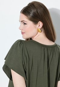 Vihreä oliivinvihreä, löysä toppi lyhyillä hihoilla ja koottu kaula-aukko. Kultasävyt, uritettu soikea korvakorut täydentävät asun.