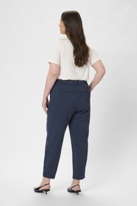 Pantalones tapered en color navy con cintura elástica, que cuentan con dos bolsillos traseros. Combinados con una blusa de manga corta en color beige claro.