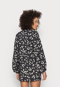 Vestido preto com pequeno padrão floral branco, mangas bufantes longas, gola alta e um corte relaxed. Tecido suave com ligeiro brilho e detalhes franzidos.