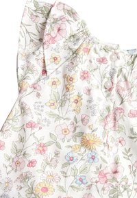 Una tela con estampado floral presenta flores en tonos rosa, amarillo y azul sobre un fondo claro, con un volante fruncido y botones en el escote.