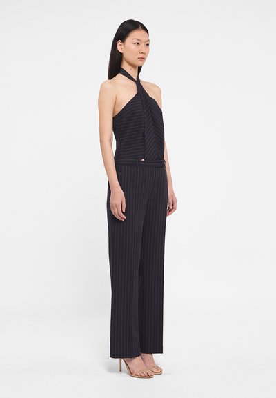 Námornícky pruhovaný halter top s skrúteným výstrihom, kombinovaný s obnovenými, širokými nohavicami. Model má na sebe minimalistické telové opätky.