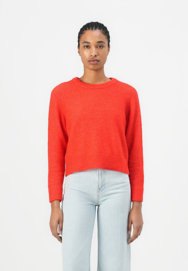 Rode cropped trui met lange mouwen, ronde hals en geribbelde manchetten, gecombineerd met lichtblauwe high-waisted jeans.