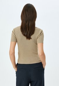 Beige ribbad kortärmad topp med en åtsittande design, kombinerad med mörka randiga byxor. Tyget verkar mjukt och strukturerat.