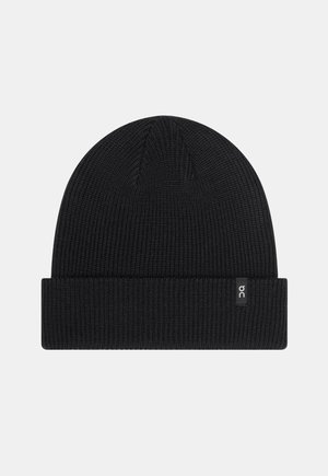 Gorro de punto negro con dobladillo, que presenta una pequeña etiqueta de logo blanca en el lado. Textura suave y ajuste redondeado ceñido.