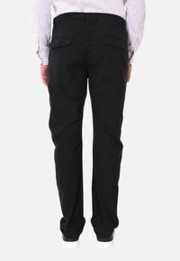 Pantaloni neri in cotone con design a gamba dritta, tasche posteriori e finitura pulita. Accompagnati da sneakers bianche.