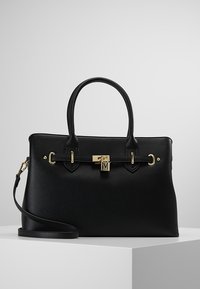 Svart läderhandväska med guldfärgade detaljer, korta handtag och ett avtagbart axelrem. Har en lås- och spänndesign, texturerad yta och rymligt innervärde.