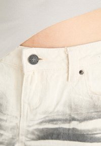 White denim pants with a faded black graphic print, featuring a silver button closure and light stitching details at the waistband.