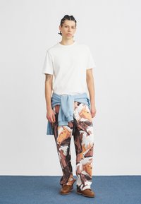 Fehér pamut póló, világoskék pulóver a derékon kötve, ló mintás barna és fehér nadrág, barna cipők.