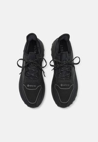 Baskets de course noires avec une tige texturée, portant la marque GORE-TEX, des lacets plats et un col rembourré. Semelle en caoutchouc crantée pour une meilleure adhérence.