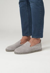 Los zapatos de ante gris de tipo slip-on presentan una puntera redonda, paneles laterales elásticos y una suela de cuerda de yute con costura decorativa a lo largo del borde.