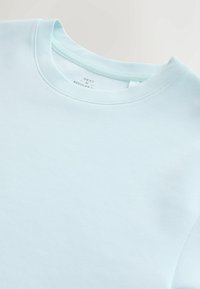 T-shirt bleu clair à col rond avec couture visible au niveau du col et étiquette de taille imprimée à l'intérieur du col.
