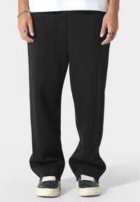 Czarne dresy w luźnym kroju, z bocznymi szwami, gładką teksturą, w połączeniu z czarnymi butami na białych sznurowadłach.