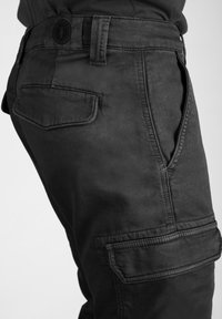 Pantalones cargo negros hechos de una tela de textura suave, con bolsillos laterales y traseros, pasadores para cinturón y detalles de costura reforzada.