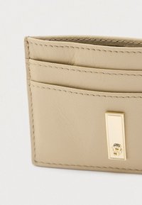 Portacarte in pelle beige con quattro scomparti per carte, bordi cuciti e un dettaglio hardware rettangolare color oro sul davanti.