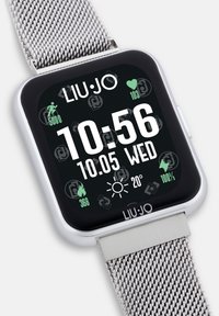 Silbernes Netzarmband-Smartwatch mit schwarzem Ziffernblatt, das Uhrzeit, Datum und Gesundheitsdaten anzeigt. Hat ein quadratisches Design und ein auffälliges Markenlogo.