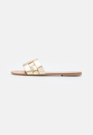 Flat slide sandal with metallic gold woven strap and tan sole, viewed from the side on a neutral background.