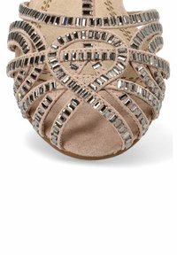 Sandalia beige con múltiples correas trenzadas adornadas con acentos metálicos rectangulares y cuadrados, con una textura de tela suave y puntera abierta.