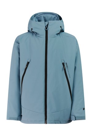 Kind trägt blaue Winterjacke und Hose, schwarze Handschuhe, schwarze Stiefel, schwarze Mütze und Skibrille auf dem Kopf, steht vor neutralem Hintergrund.