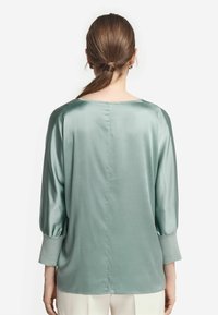Satin långärmad skjorta i mjuk grön, med avslappnad passform, rund halsringning och något puffade ärmar. Slät textur med en elegant finish.