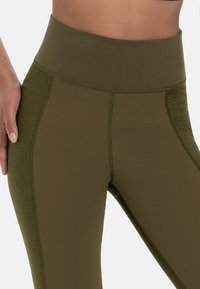 Olijfgroene high-waisted leggings met een gladde textuur, voorzien van zijpanelen en stikdetails voor extra ontwerpelementen.