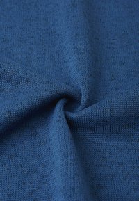 Niebieska dziana tkanina o teksturowanej, miękkiej powierzchni. Materiał ma subtelny wzór, podkreślający głęboki niebieski odcień z ciemniejszymi plamkami.