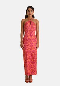 Vestido maxi rosa colorido con cuello halter y un intrincado patrón púrpura; presenta un diseño ajustado y una textura sutil. Sandalias de plataforma apiladas.